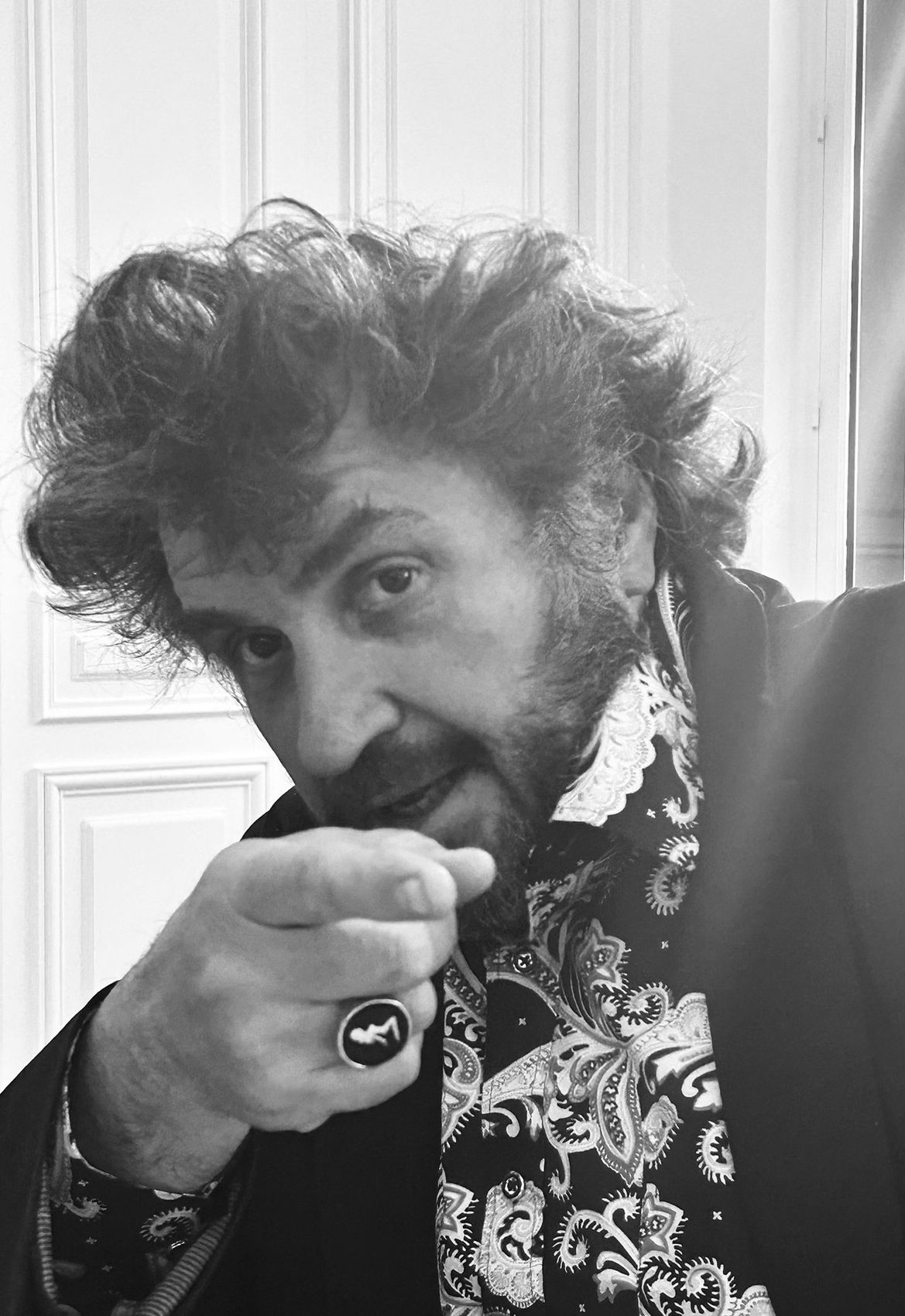 Frédéric Roulette de face, cheveux en bataille, chemise à motif cachemire, l'index tendu vers l'objectif